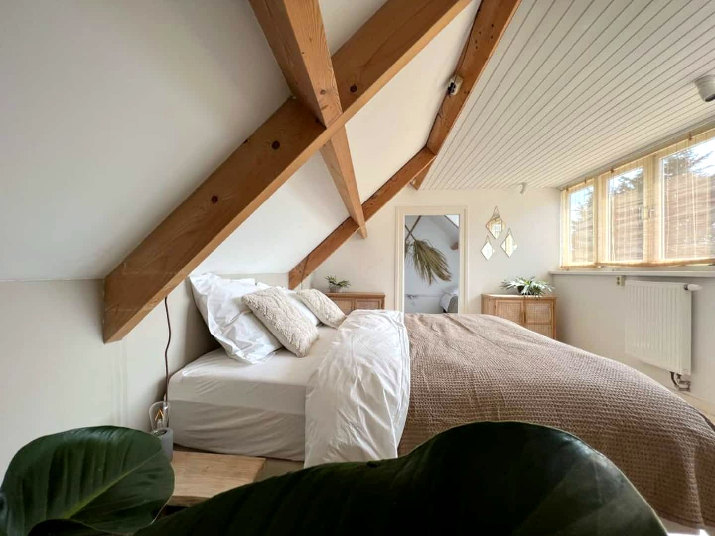 Het opgemaakte bed met kussens onder het schuine dak